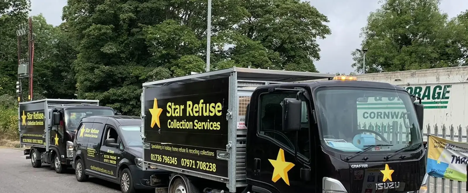 A row of black Star Refuse collection trucks and a van, liveried with the amber star logo, parked beside a tree-lined road
